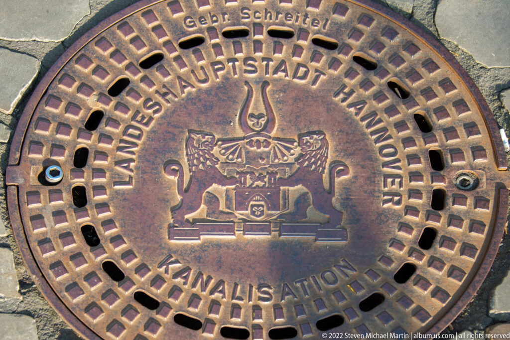 Round metal sewer cover reading “Landeshauptstadt Hannover” and “Kanalisation” around a central civic emblem.