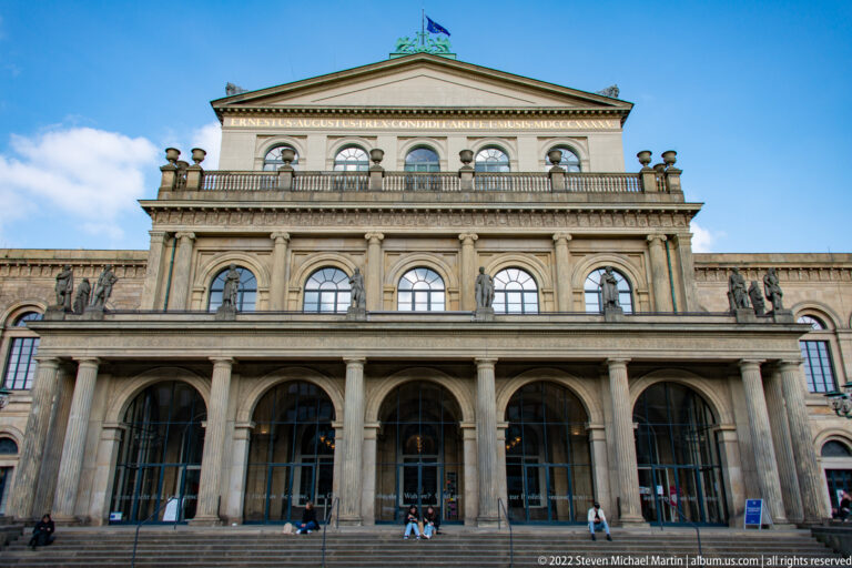 Frontal view of Staatsoper Hannover with three entrance arches, terrace, statues, and triangular pediment.