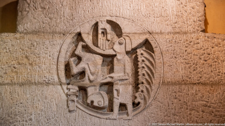 Circular weathered stone relief with a stylized armored or heraldic figure carved into a masonry wall.