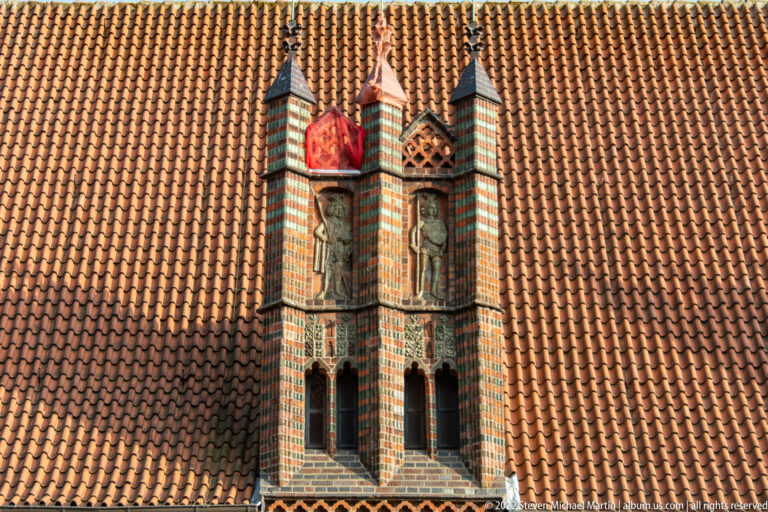 Pair of narrow decorative brick turrets with pointed caps and a red shield motif rising from a clay-tiled roof.