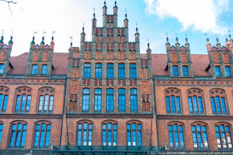 Ornate red-brick stepped gable with grouped windows, patterned masonry, pinnacles, and decorative pointed panels.