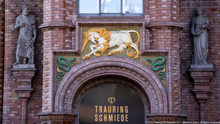Arched brick doorway topped by a white lion on gold, green serpentine ornaments, and stone figures in side niches.