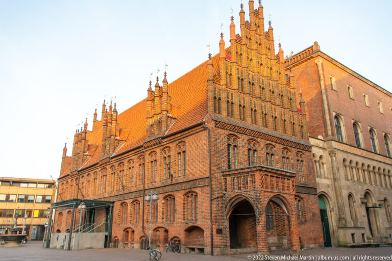 Large red-brick civic building with multiple stepped gables, tall windows, tiled roofs, and an arched passage.