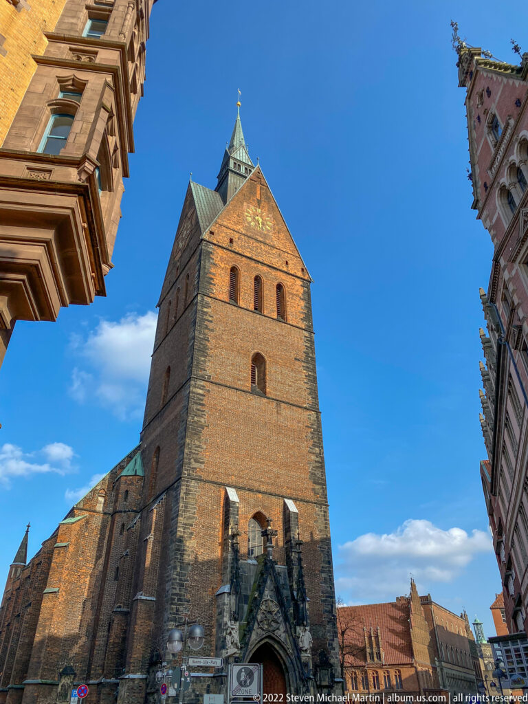 Massive brick tower of Hannover’s Marktkirche seen from below against a bright blue sky.