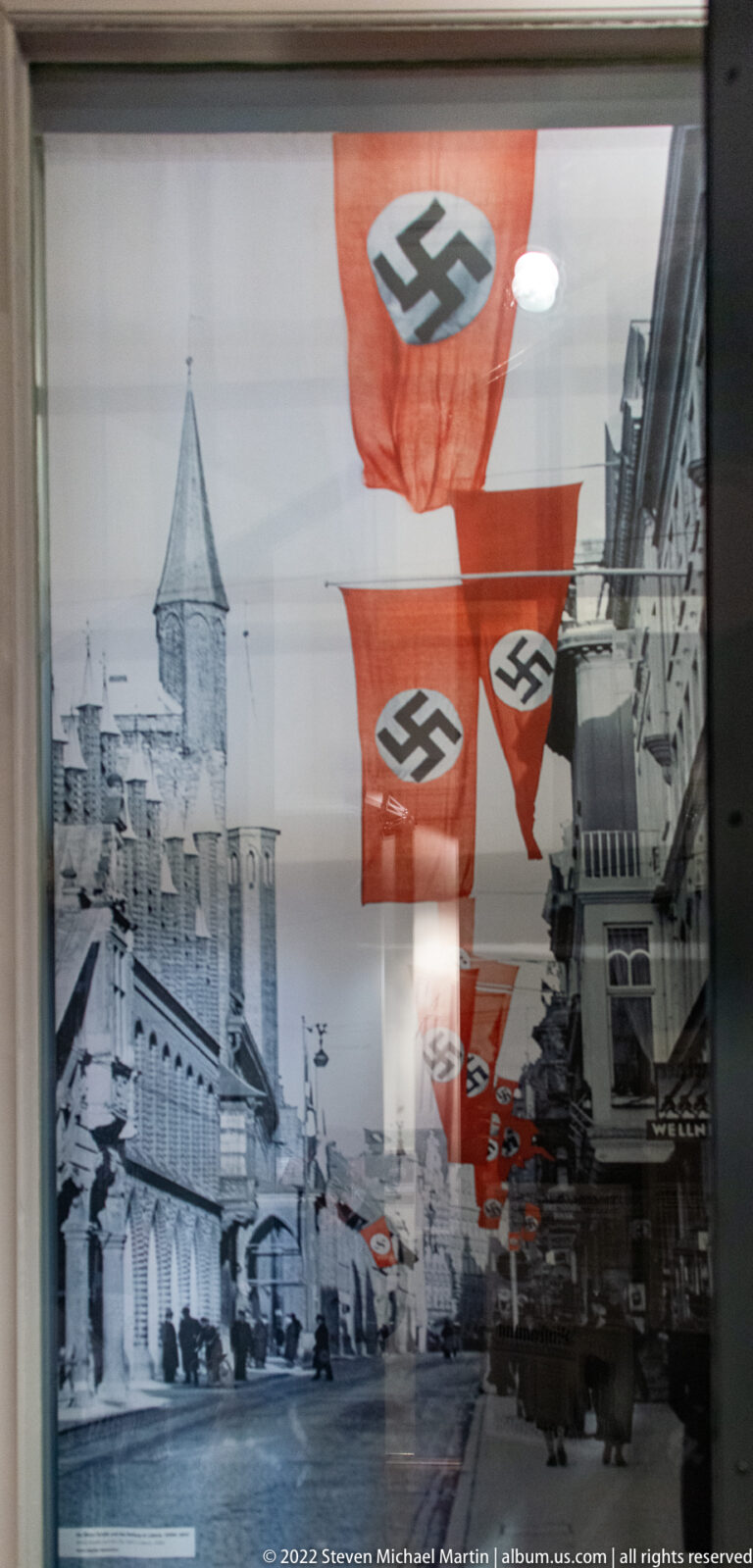 Black-and-white historic Lübeck street photograph with multiple large swastika flags hanging above the roadway.