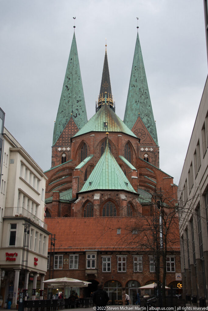 Large red-brick church with polygonal chapels, green copper roofs, and twin towers rising behind the eastern end.