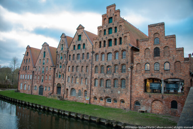 Row of tall historic brick salt warehouses with stepped gables beside the Trave waterfront in Lübeck.