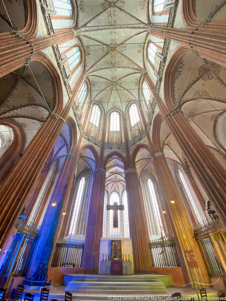 Upward interior view of a Brick Gothic church with tall red-brick piers, pointed windows, and pale decorated vaults.