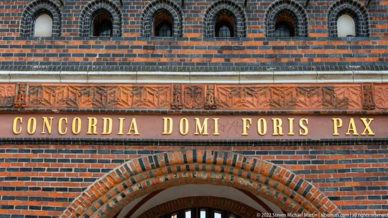 Gold letters reading “CONCORDIA DOMI FORIS PAX” across patterned Holstentor brickwork above an arch.