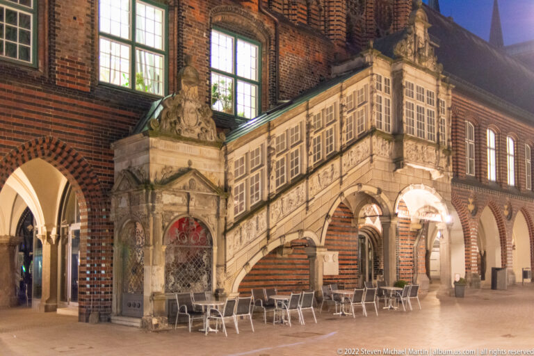 Ornate Renaissance stone staircase of Lübeck Town Hall on Breite Straße, with carved balustrades, heraldic decoration, and brick arcades.