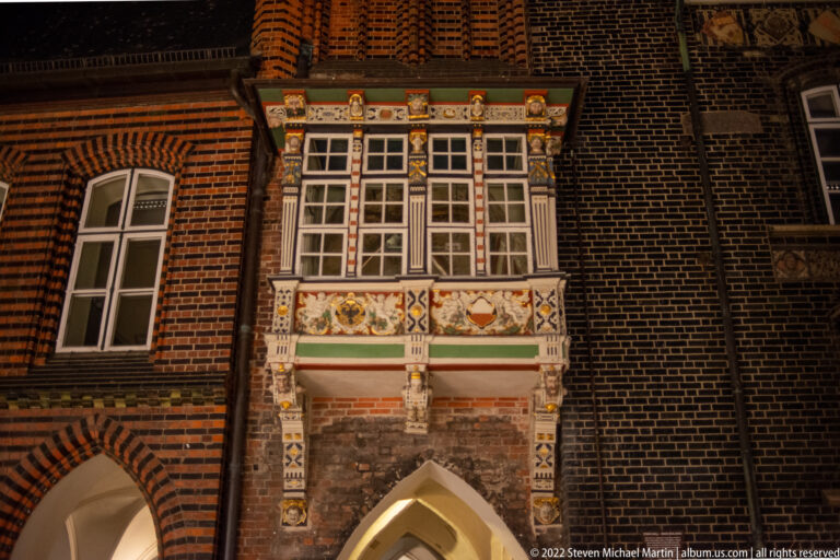 Decorated Renaissance wooden oriel on Lübeck Town Hall, with small-paned windows, painted panels, carved figures, masks, and heraldic ornament.
