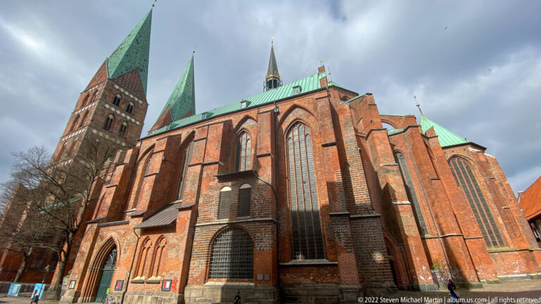 North-side exterior of St. Mary’s Church in Lübeck, with red-brick buttresses, tall Gothic windows, green copper roofs, tower, and roof turret.