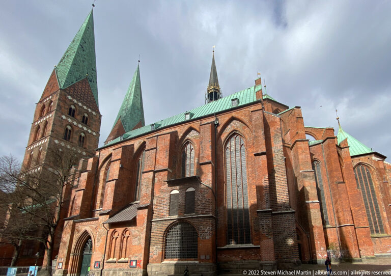 Side view of St. Mary’s Church in Lübeck with massive brick buttresses, tall pointed windows, green copper roofs, and western tower.