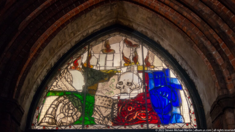 Markus Lüpertz’s 2002 tympanum window in St. Mary’s Dance of Death Chapel, centered on a skull with dove, rose, fish, blue vessel, and flames.