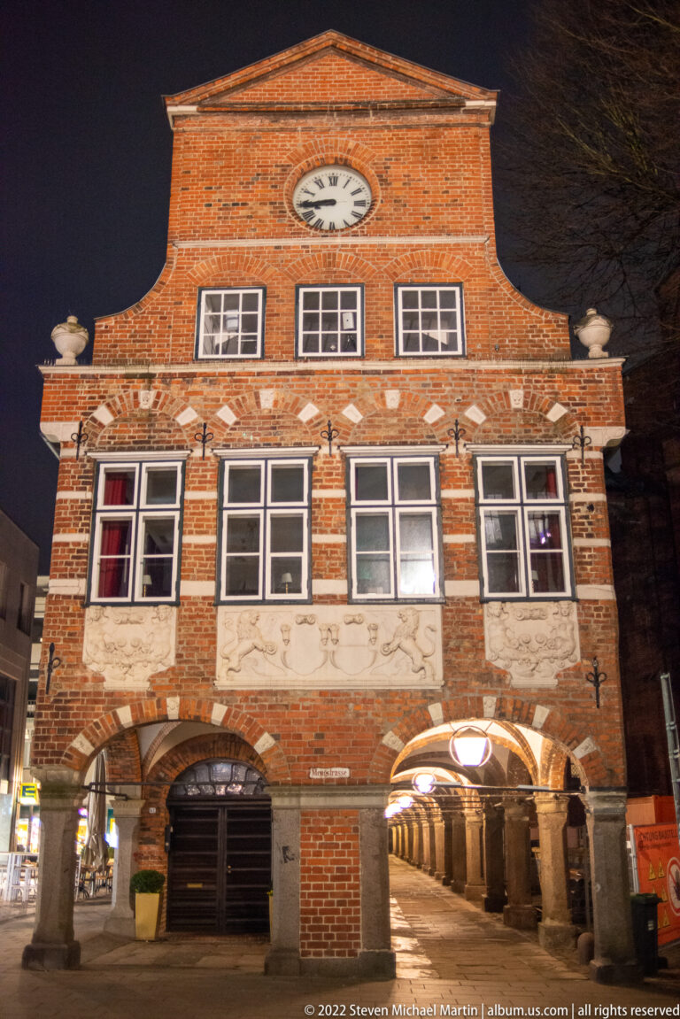 Clock-gabled brick wing of Lübeck’s Heiligen-Geist-Hospital with white-framed windows, decorative bands, and an arched passage.