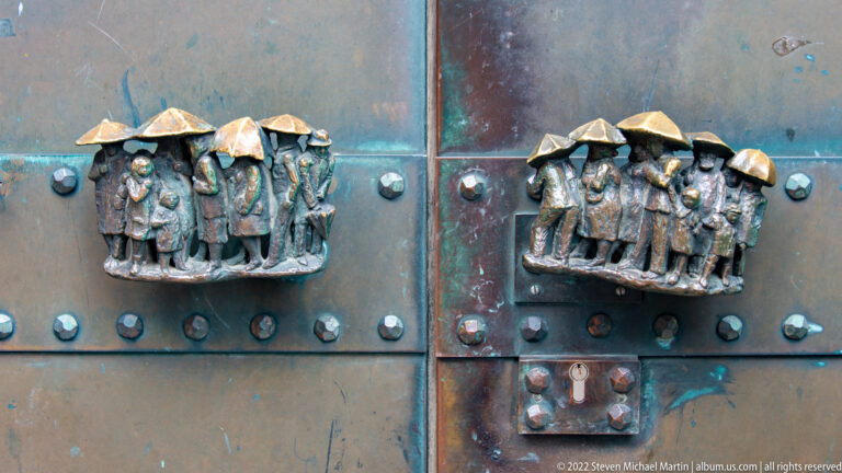 Patinated metal church door with two figural bronze fittings, rows of rivets, and green-blue oxidation.