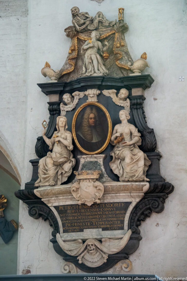 Large Baroque wall epitaph with central portrait, sculpted figures, dark frame, and inscribed memorial tablet.