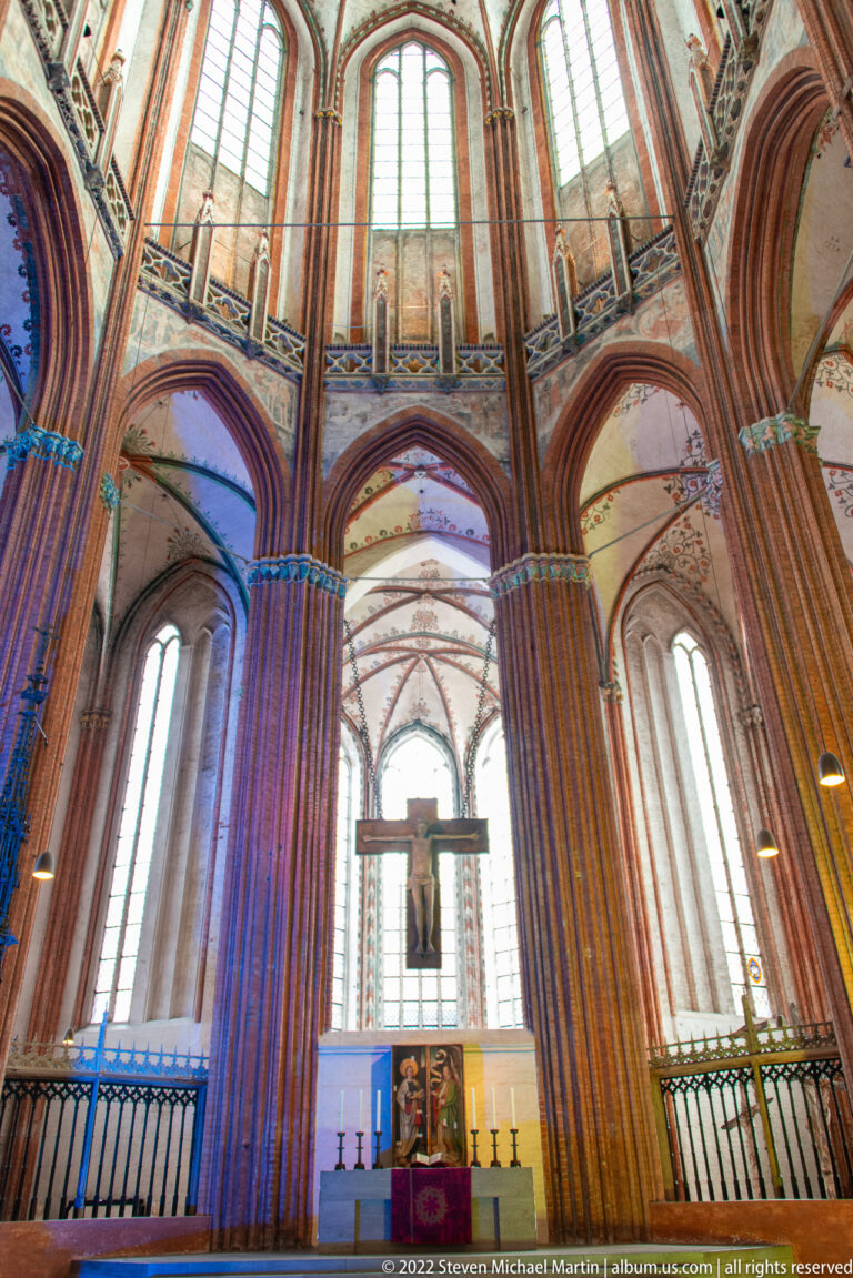 Tall Brick Gothic church bay with clustered red-brick piers, pointed arches, large windows, altar, and blue accent light.