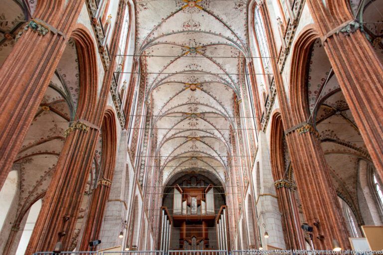 Long Brick Gothic nave with red-brick arcades, painted rib vaults, and a pipe organ centered at the far end.