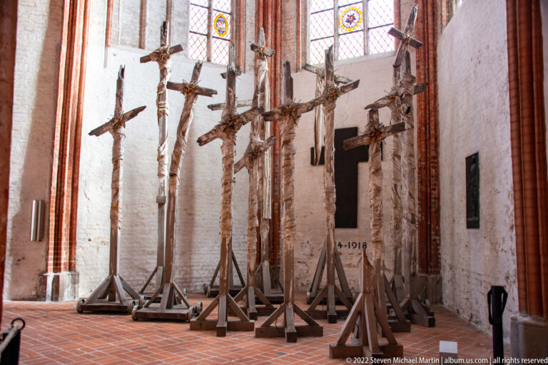 Several large crucifixes with carved figures of Christ displayed in a row on freestanding wooden supports inside a church.