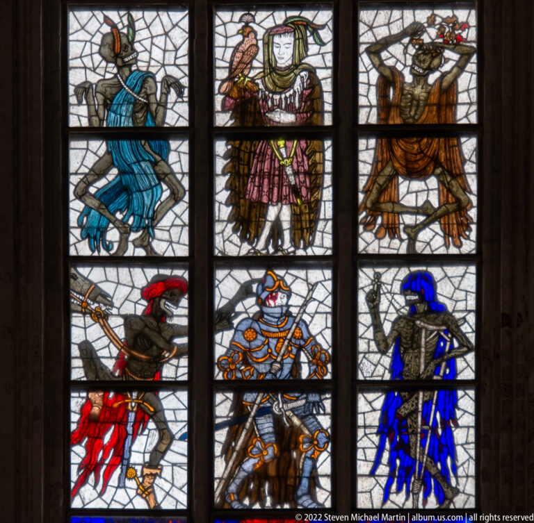 Armored and courtly figures with skeletal companions in Alfred Mahlau’s vertically arranged Dance of Death stained-glass window.