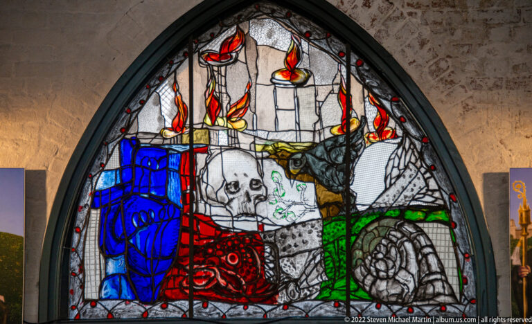 Markus Lüpertz’s 2002 tympanum window with skull, dove, fish, blue vessel, snail-like form, rose, and flame motifs.