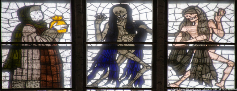 Three figures in Alfred Mahlau’s Dance of Death stained glass, including a central skeletal Death figure between two living or corpse-like figures.