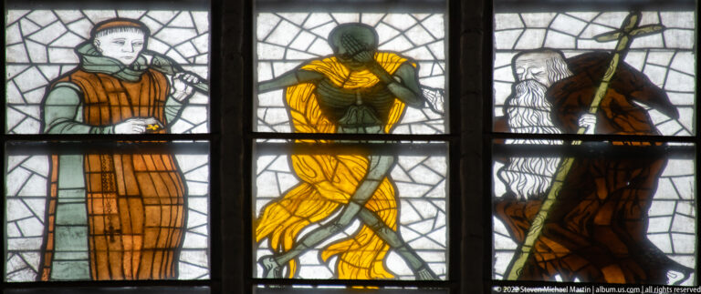 Yellow-clad living figure bending between gaunt Death figures in Alfred Mahlau’s 1956/57 Lübeck Dance of Death window.