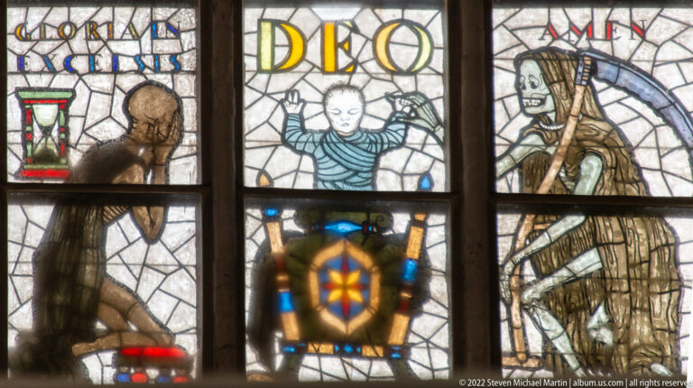 Final section of Alfred Mahlau’s Dance of Death window with the blessing Christ Child, Death figures, and “AMEN” inscription.