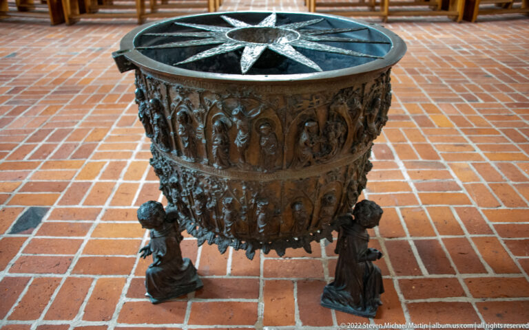 Large dark bronze basin on sculptural feet, decorated with relief figures and topped by a broad circular surface with star motif.