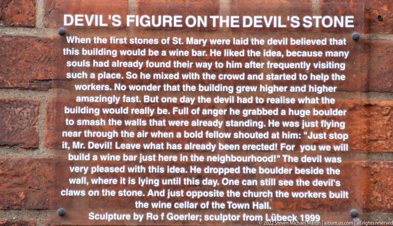 Brick-mounted interpretive plaque describing the Devil's Stone legend and a devil sculpture near St. Mary's Church.