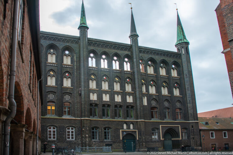Dark brick Neo-Gothic façade with repeated pointed windows, slender pinnacles, and a central arched entrance.