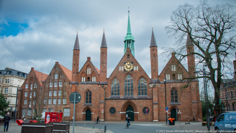 Brick Gothic Heiligen-Geist-Hospital with multiple steep gables, slender turrets, central clock, and arched entrances.