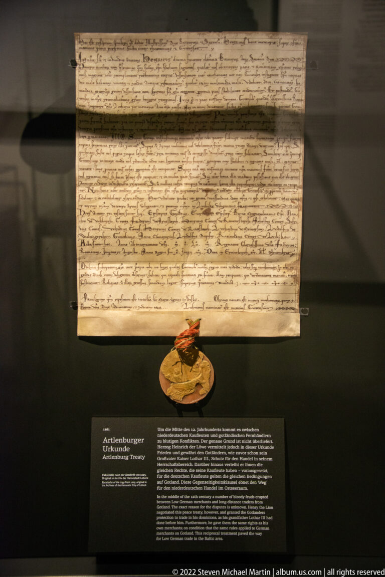 Handwritten parchment document with a pendant seal displayed above an interpretive museum label.
