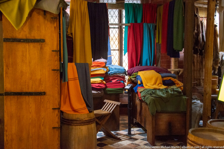 Reconstructed historic room with brightly colored textiles, wooden chests, barrels, benches, and leaded windows.
