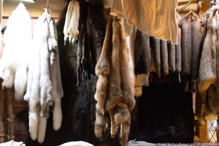 Hanging animal pelts in white, tan, brown, and dark fur arranged as a museum trade-goods display.