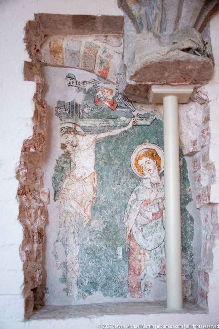 Fragmentary wall painting of haloed figures on a blue-green ground, surrounded by exposed brick and plaster losses.