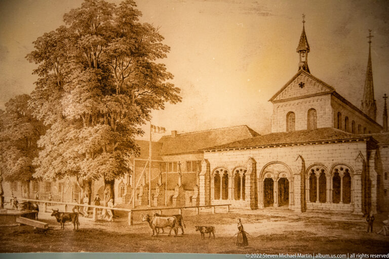 Sepia historical illustration of an arcaded monastery building with a square tower, distant spire, cattle, and figures.