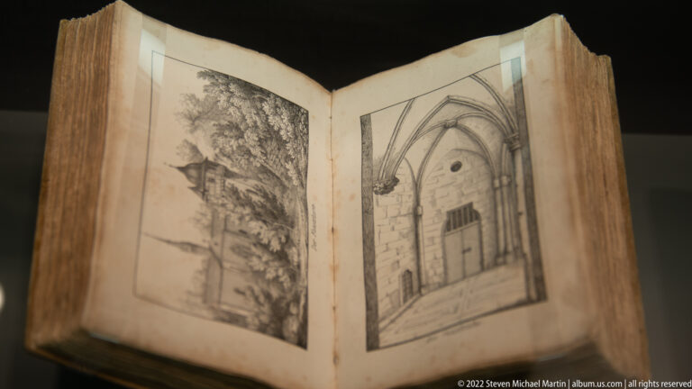Open aged book displaying two monochrome architectural illustrations, including a pointed-arched doorway or interior view.