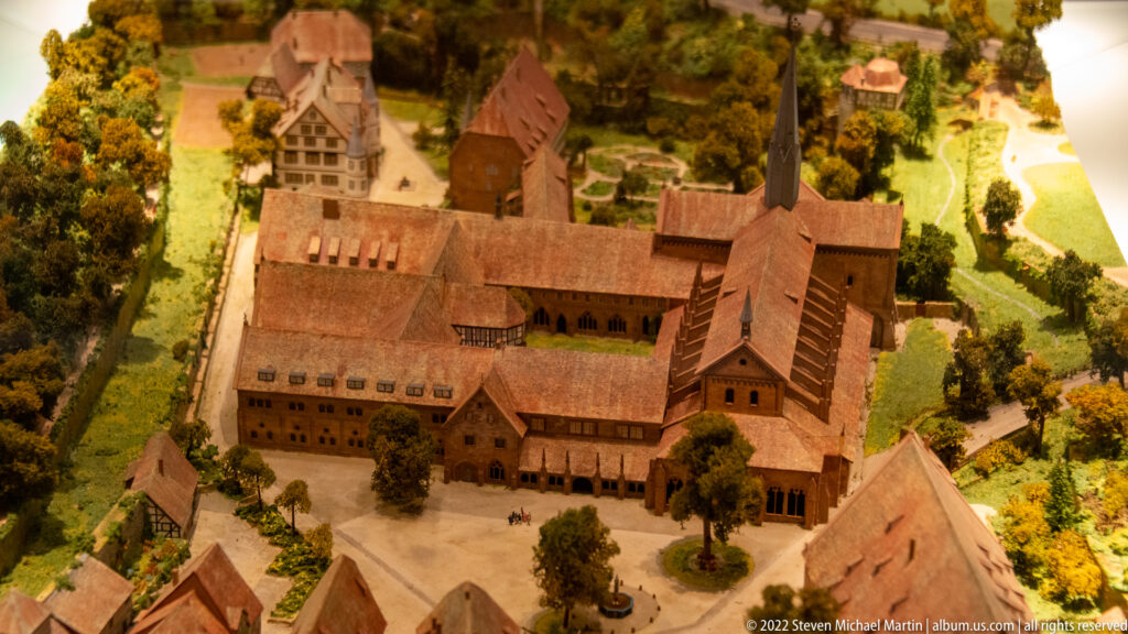 Close overhead view of a scale model showing the monastery church, cloister ranges, courts, and red tiled roofs.