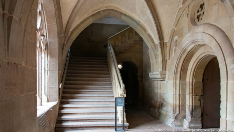 Broad stone staircase rising beneath a pointed arch beside a smaller arched doorway in a vaulted monastic passage.