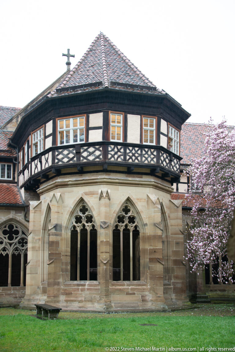 Polygonal stone bay with paired Gothic windows, topped by a timber-framed upper story and balcony.