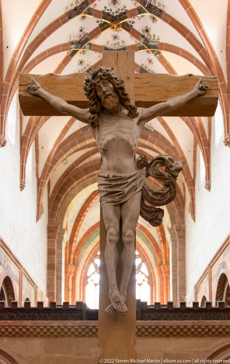 Carved figure of Christ on a wooden crucifix, seen against the rib-vaulted church ceiling.