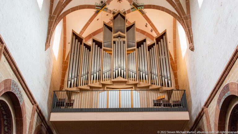 Large symmetrical pipe organ on a gallery beneath red-and-white church vaulting.