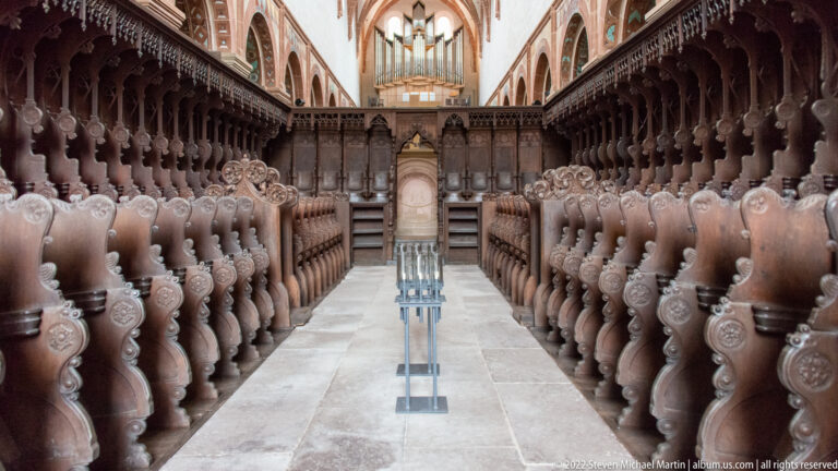 Symmetrical rows of elaborately carved wooden choir stalls flanking a central stone aisle.