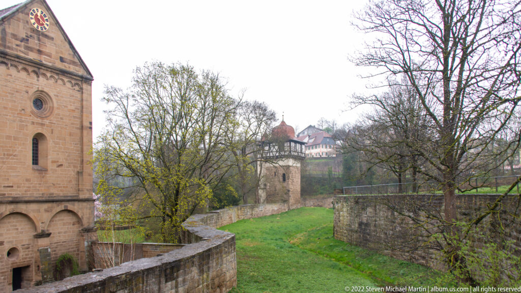 Historic stone walls, a tower, and red-roofed buildings enclosing a green precinct at Maulbron.