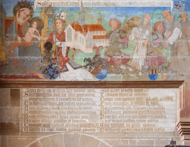 Colorful narrative mural with grouped figures above a long inscribed stone panel.