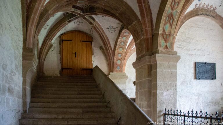 Stone steps rise to a wooden door beneath ribbed arches with traces of painted decoration.