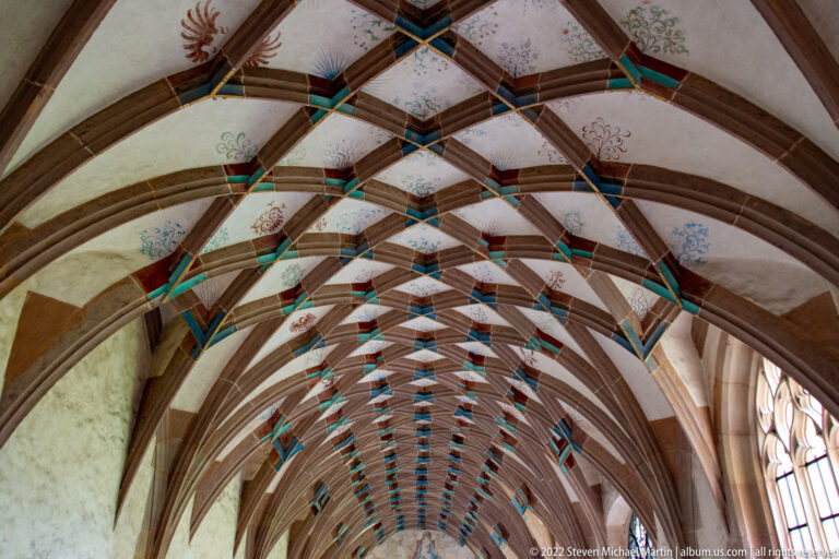 Long painted rib vault with turquoise and blue accents and faint floral decoration on pale plaster.