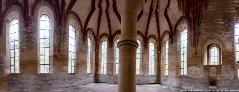 Vaulted polygonal room with a central stone column and a ring of tall pointed windows.